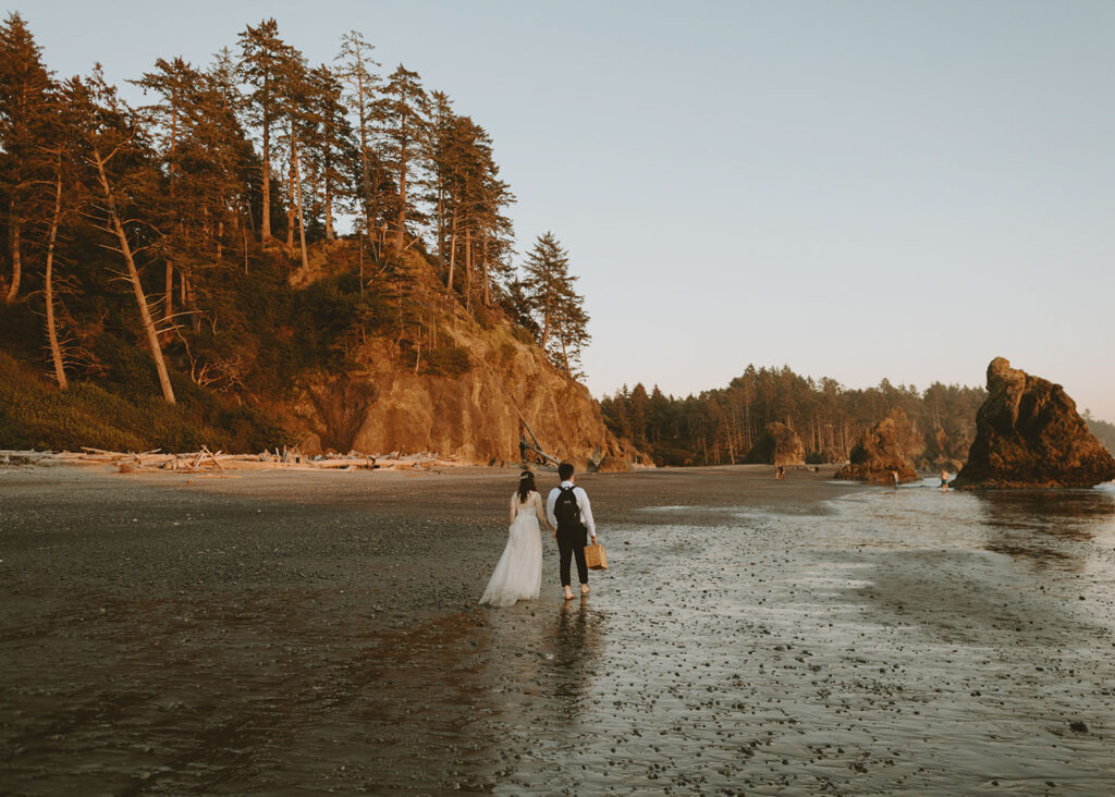 Couple walking along Oregon coastline surrounded by sea stacks