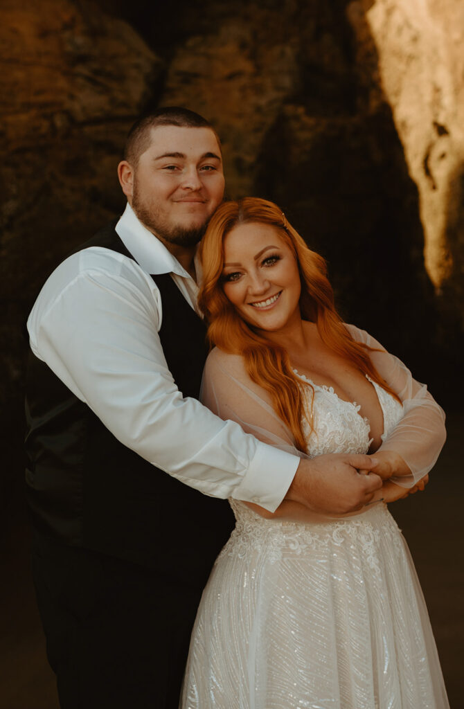 Groom hugging bride under warm light at Oregon beach