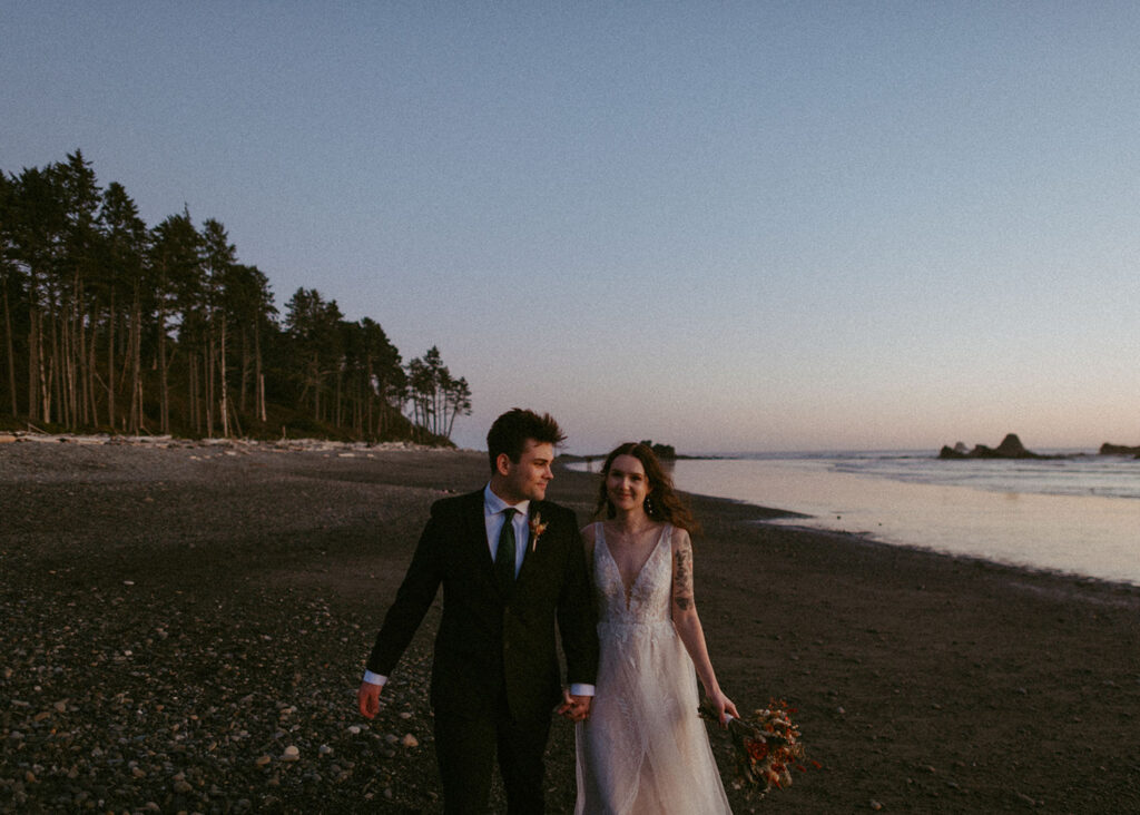 Couple walking hand in hand along rocky Oregon beach at twilight