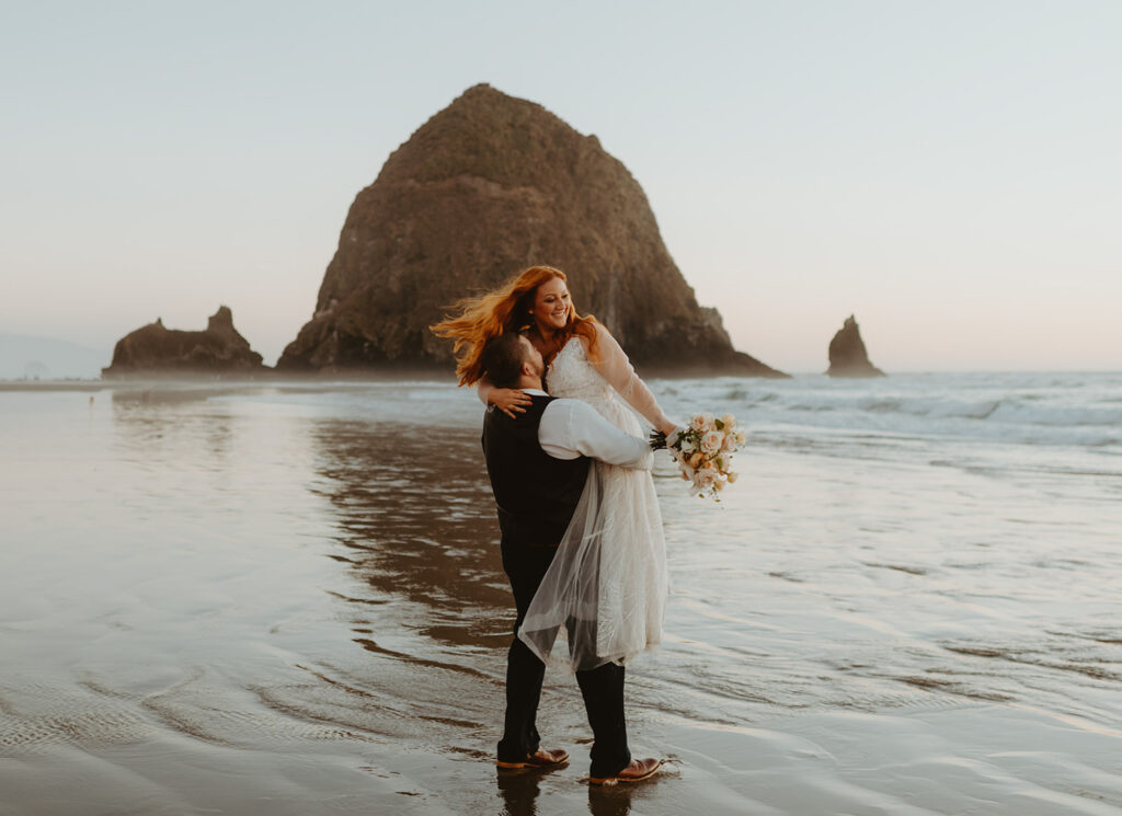 Groom lifting bride on the beach at Cannon Beach with Haystack Rock