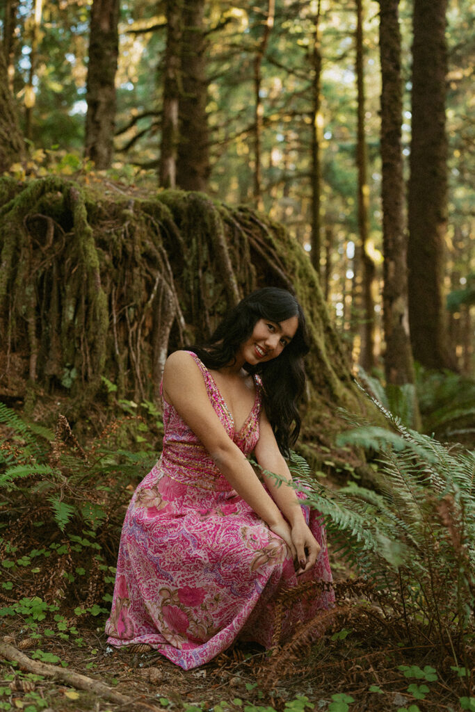 Woman in pink dress sitting near mossy tree roots
