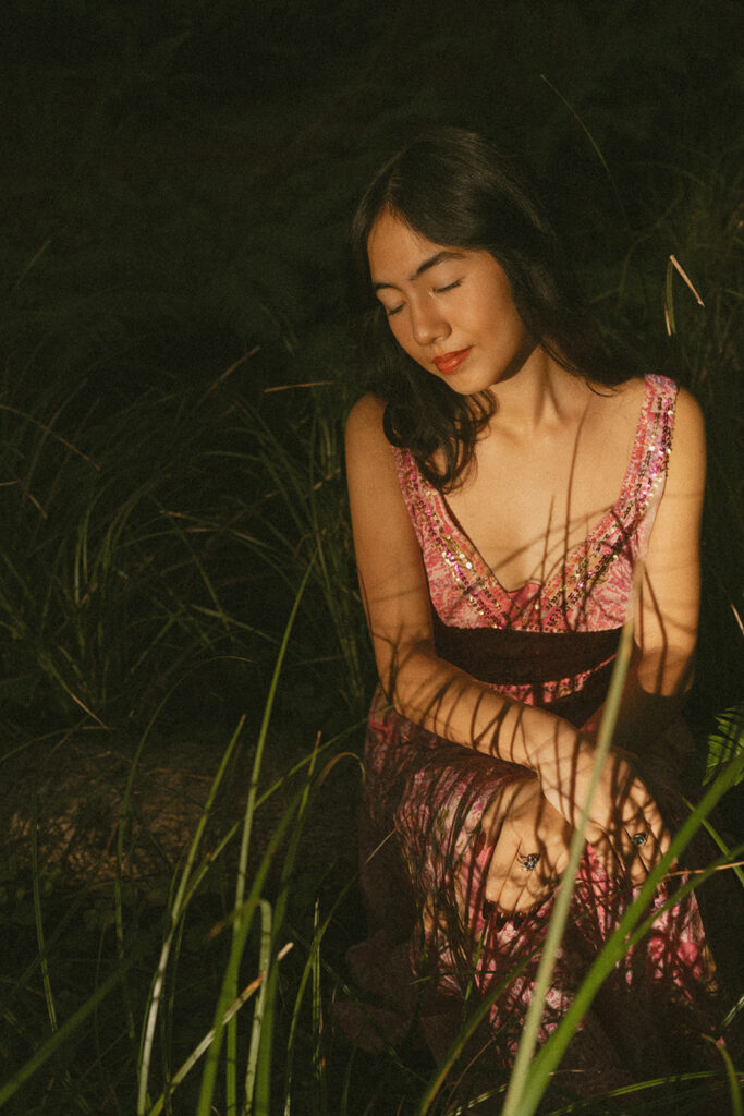 Woman in pink dress sitting with eyes closed among tall grass