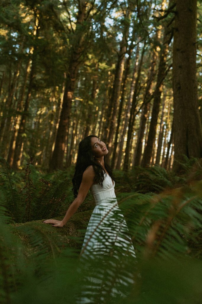 Woman in white dress looking up in forest