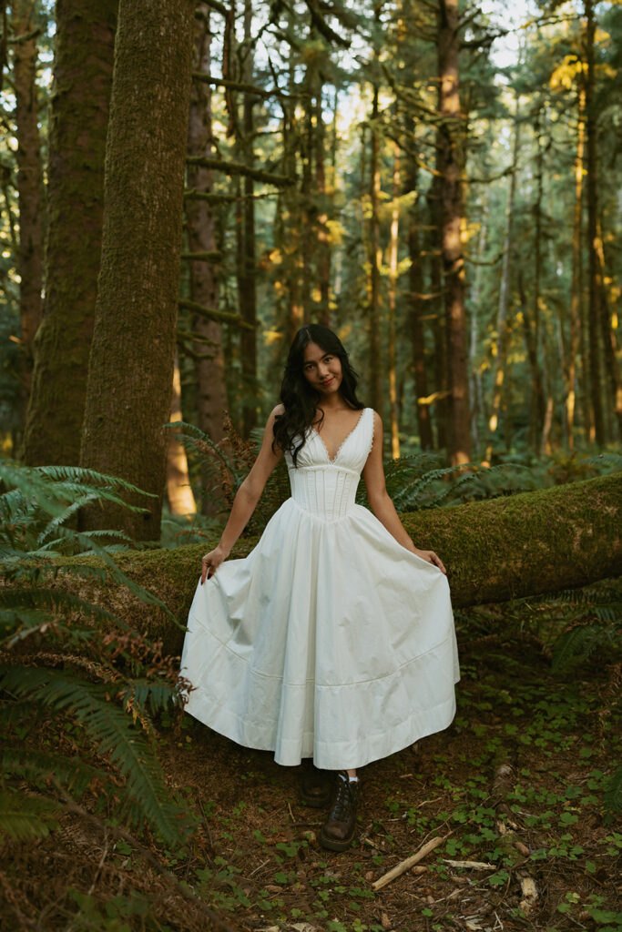 Woman in white dress posing by a mossy log in forest