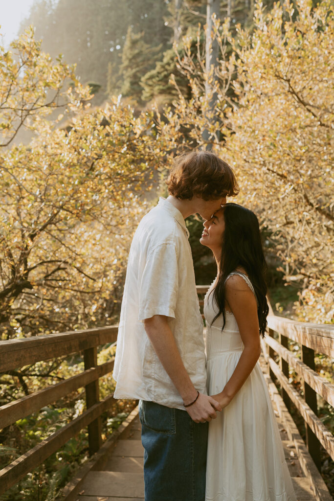 Couple holding hands on wooden bridge surrounded by trees