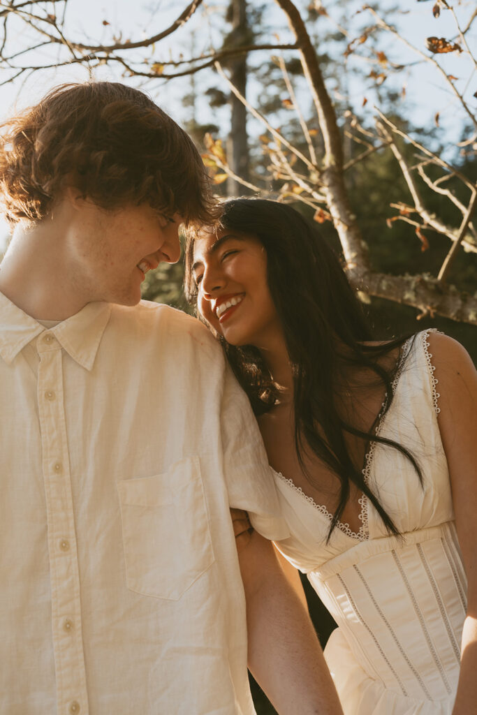 Couple smiling closely under sunlight near trees