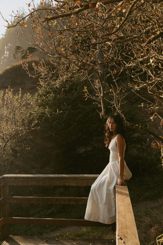 Woman in white dress sitting on wooden railing outdoors