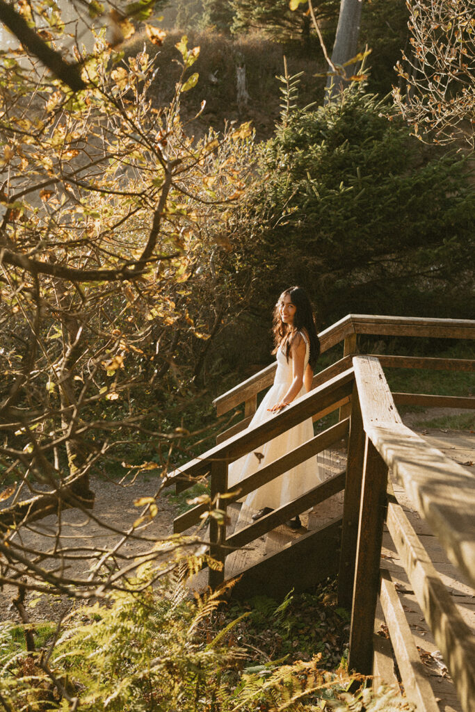 Woman in white dress standing on wooden bridge in forest