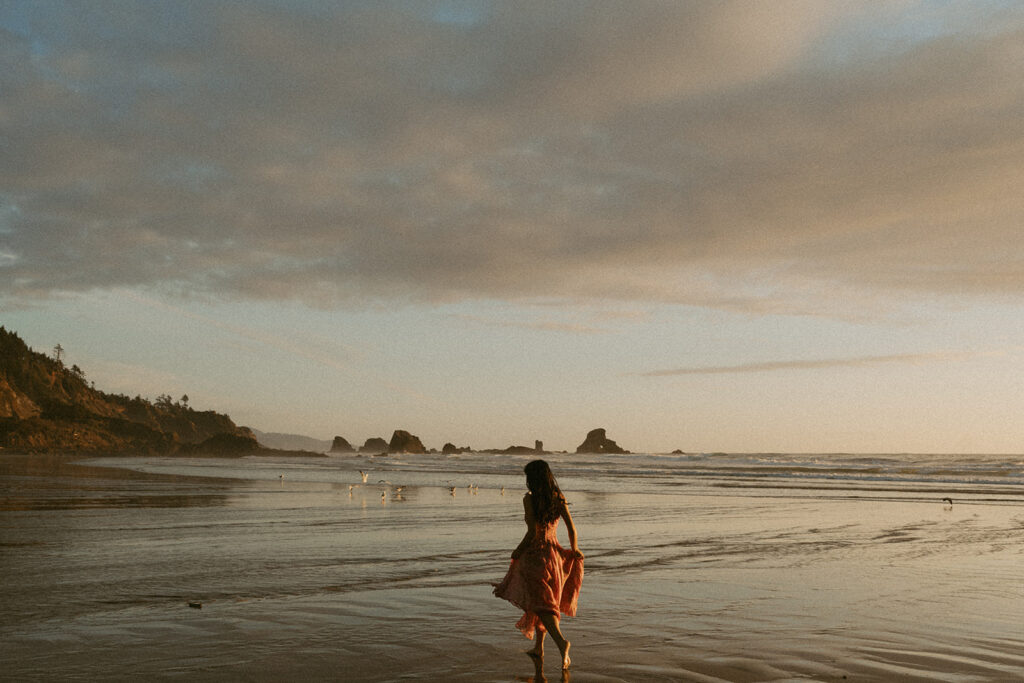 Woman in pink dress walking along the beach at sunset