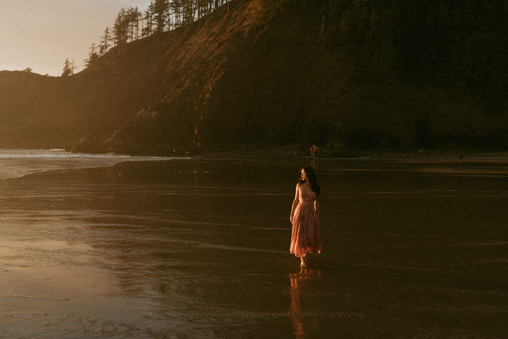 Woman in pink dress standing on wet sand with cliffs in the background