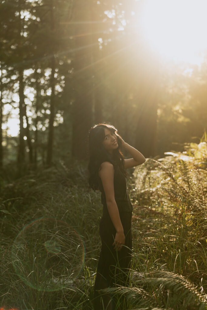 Woman in dark outfit standing in sunlight among trees