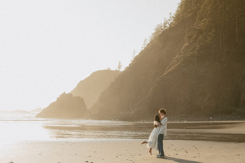 Couple embracing on beach with cliffs and sunlight in background