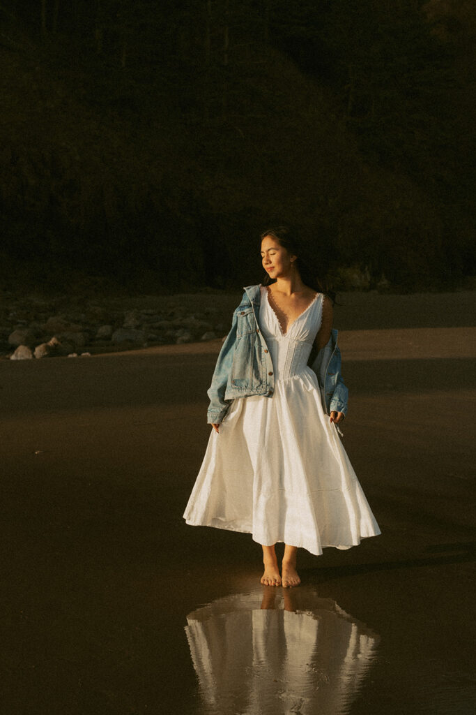 Woman in white dress and denim jacket standing on beach