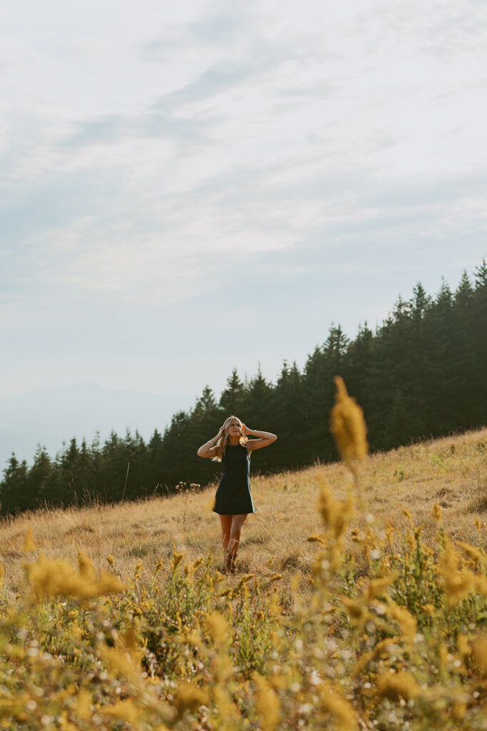 A senior stands in a field with mountain views photographed by a Salem senior photographer