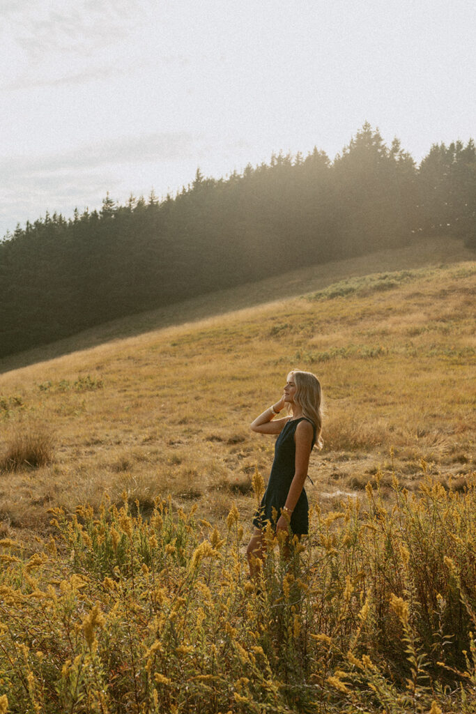 A senior girl poses in tall grass during golden hour