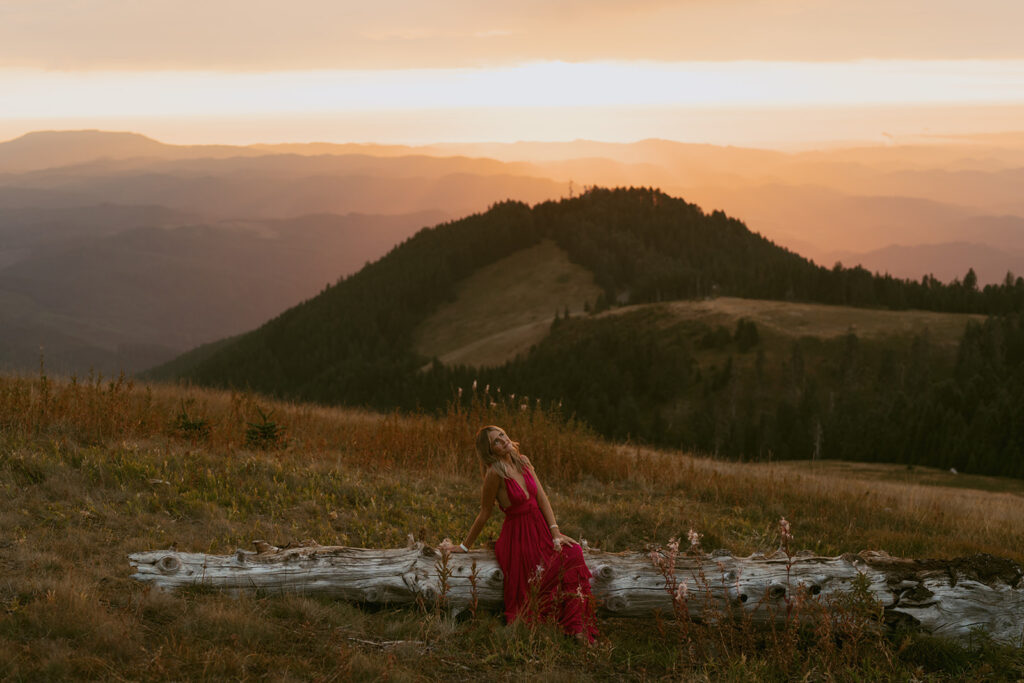 A senior sits on a fallen log at sunset with mountain views