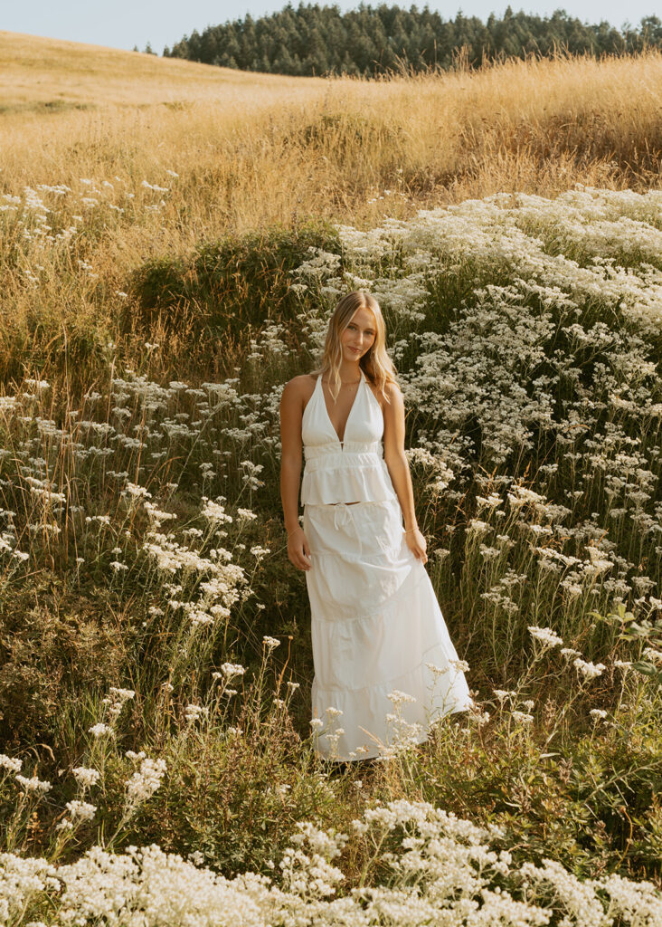 A senior girl poses with her hand behind her head in a field of wildflowers