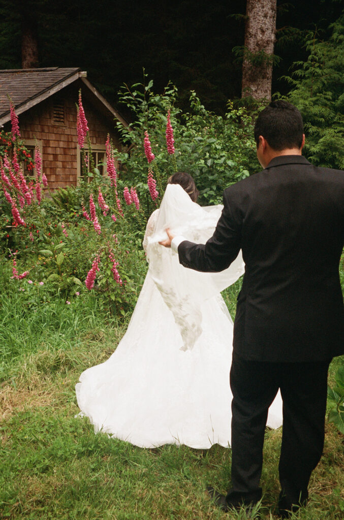 Groom lifting the bride’s veil as they walk through flowers