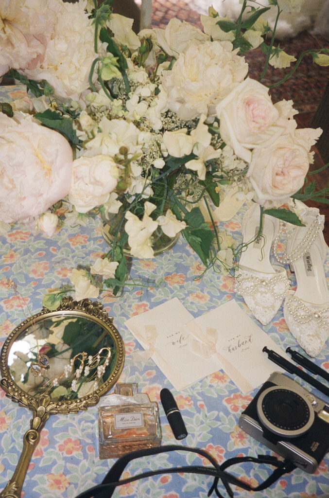 Flat lay of bridal bouquet, vow cards, jewelry, perfume, and camera.