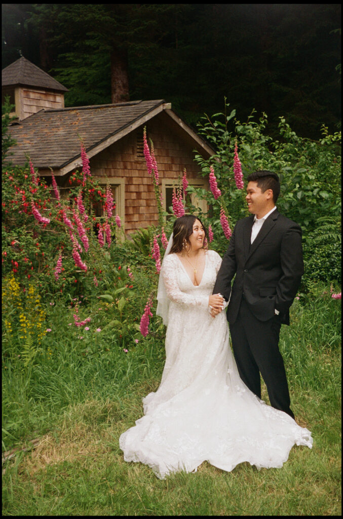 Bride and groom holding hands in a flower garden by a cottage