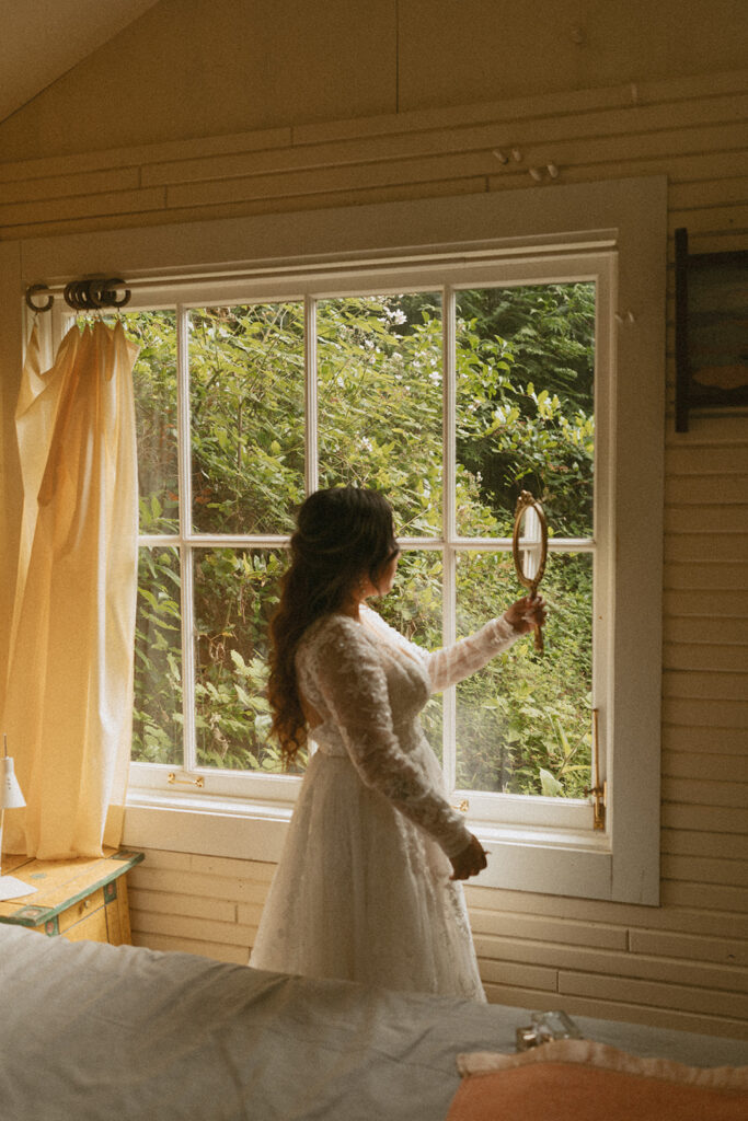 Bride holding a mirror by a cabin window
