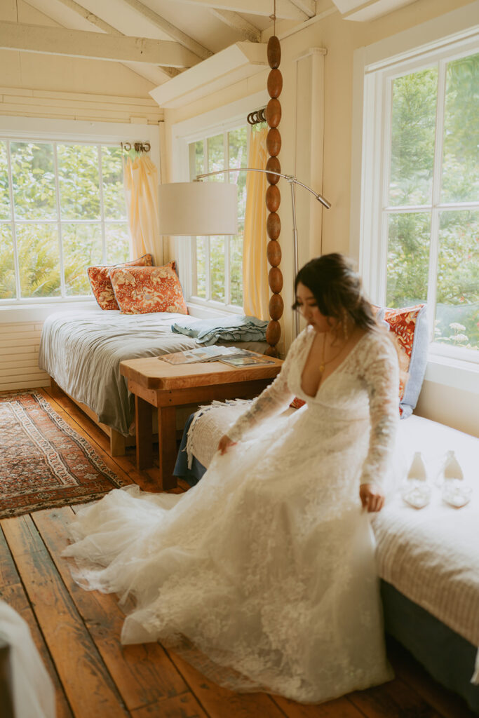 Bride in her dress sitting on a bed in a bright cabin bedroom