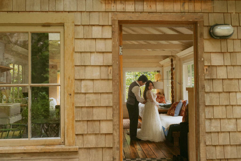 Groom helps bride with her dress inside a cabin