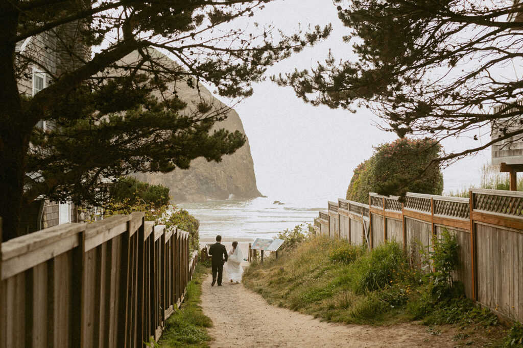 Bride and groom walking toward the beach with Haystack Rock ahead