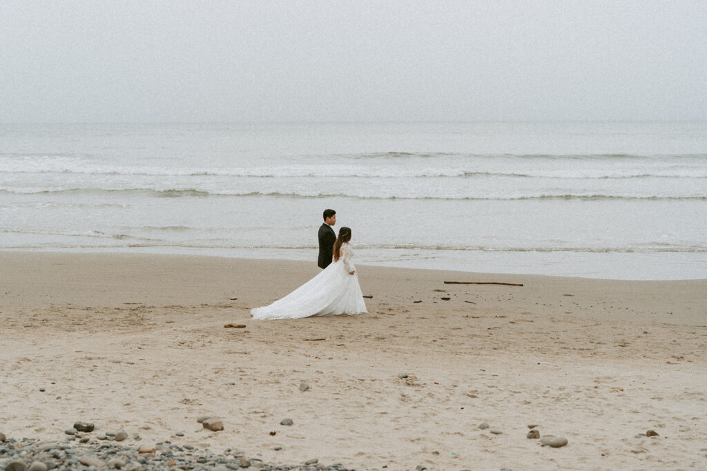 Bride and groom standing on an overcast beach with ocean waves in the background