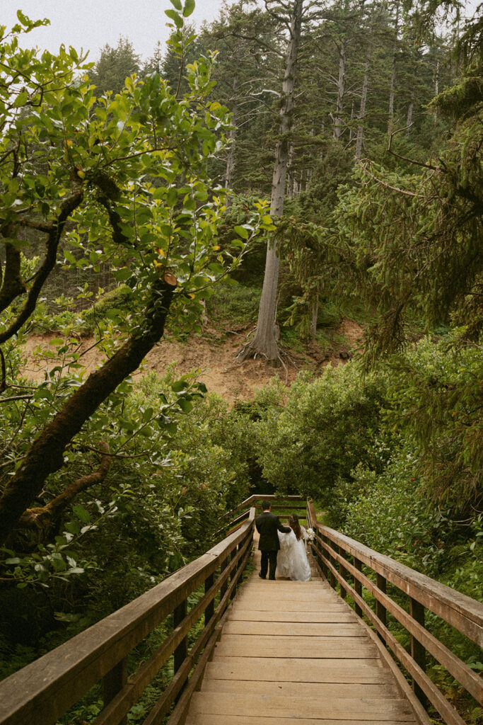 Bride and groom hiking through a fern-filled forest.