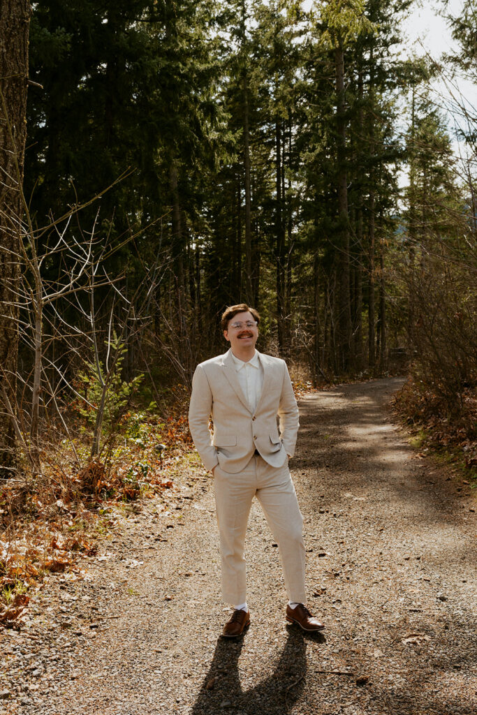 Groom in beige suit on forest path, Washington state wedding venue