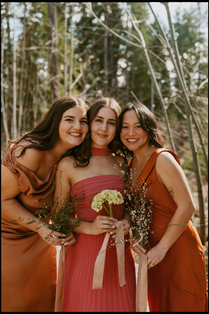 Bridesmaids in warm-toned dresses holding bouquets, forest wedding