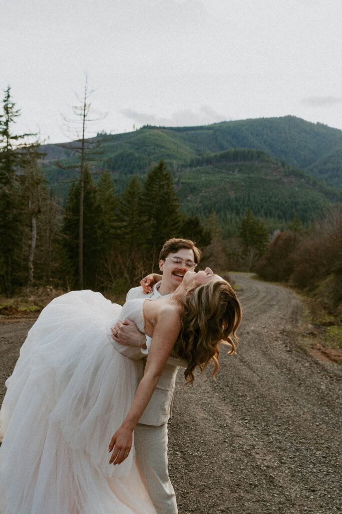 Groom dipping bride on forest road, playful pose