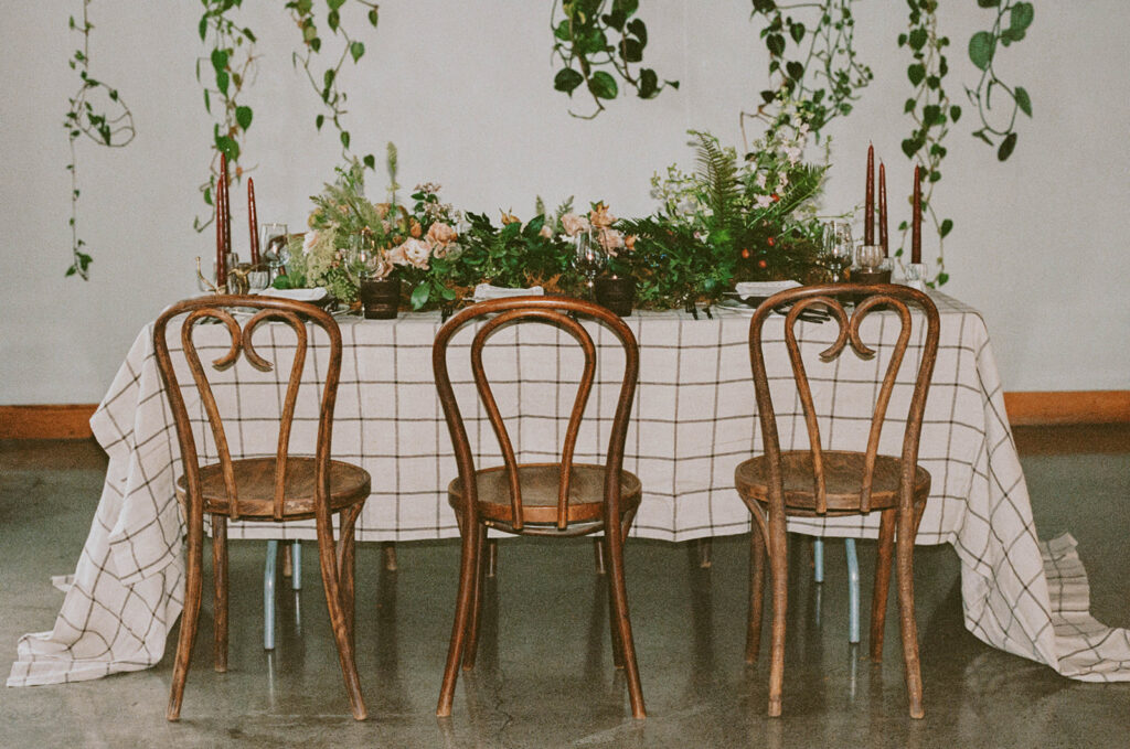 Long table setup with greenery and wooden chairs
