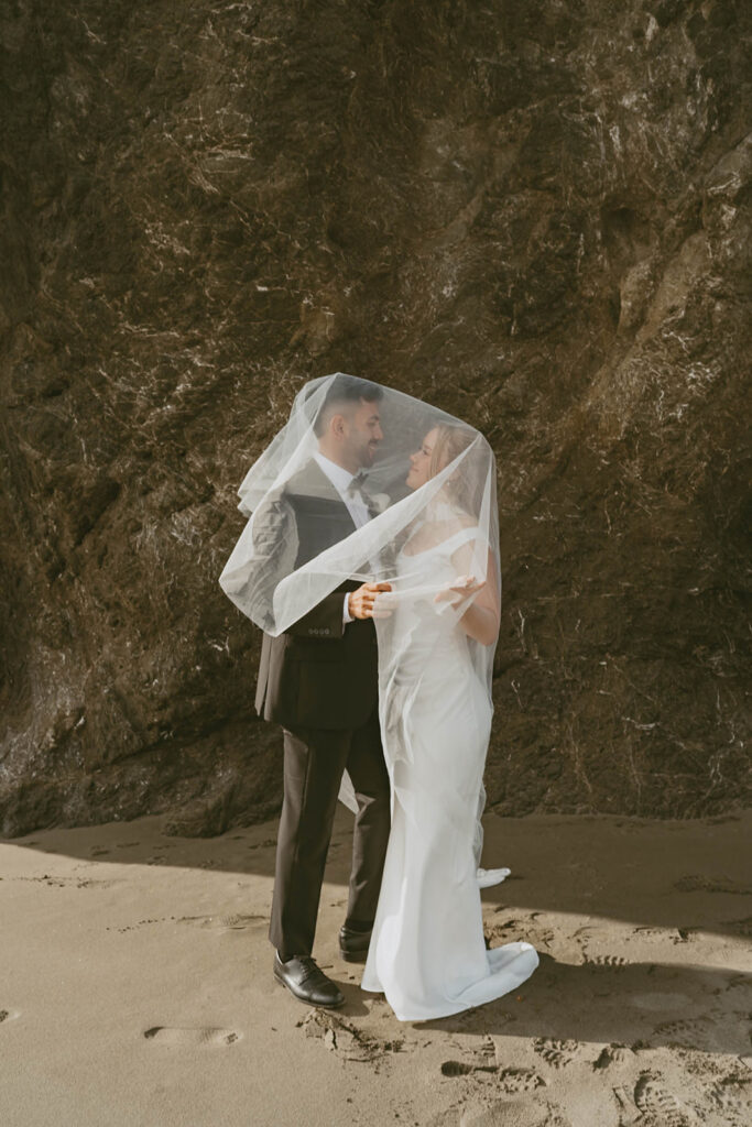 Couple standing beneath a flowing veil by a rock wall