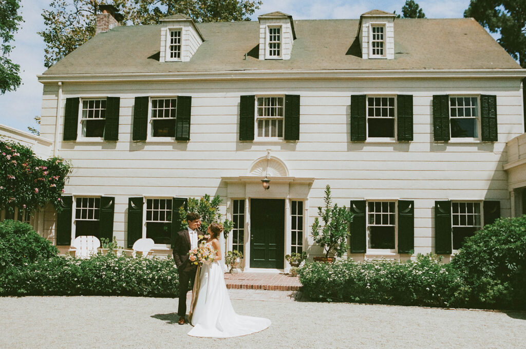Couple posing outside a white historic house