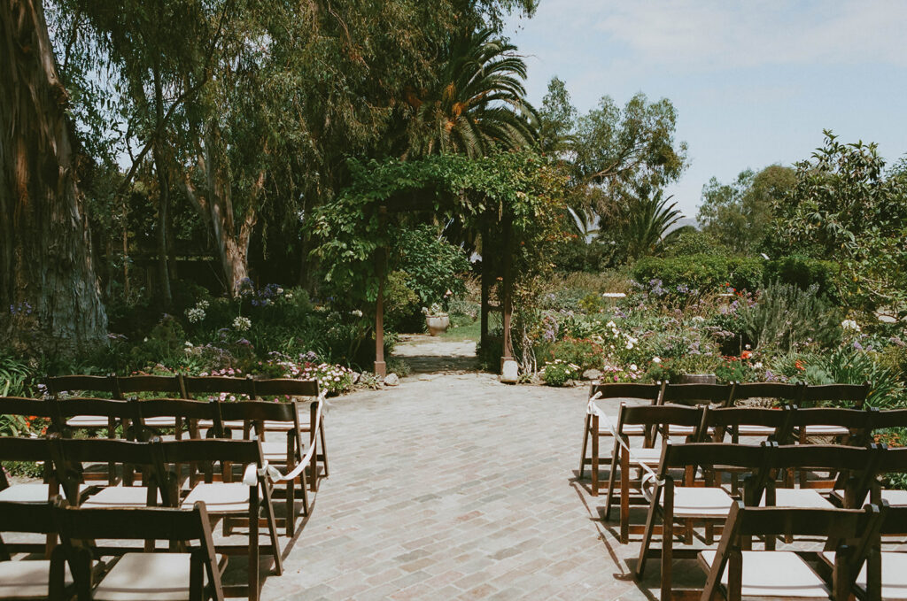 Outdoor garden ceremony setup with wooden chairs and greenery