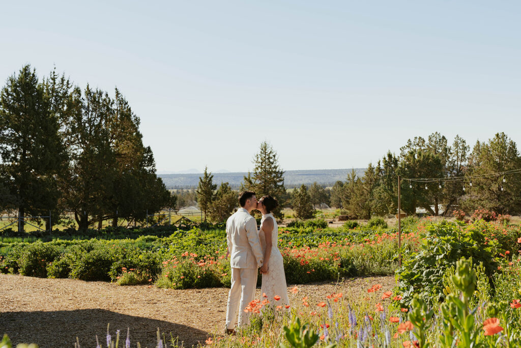 Bride and groom sharing a kiss in a garden path lined with poppies and string lights
