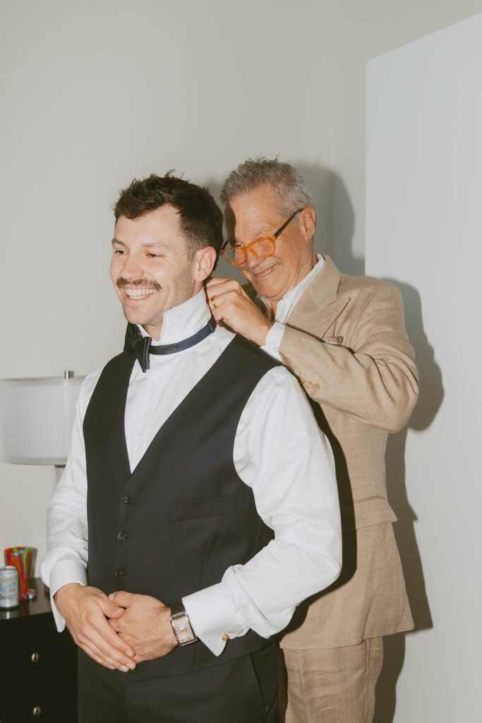 Groom's father helping him get ready, adjusting his collar before the wedding