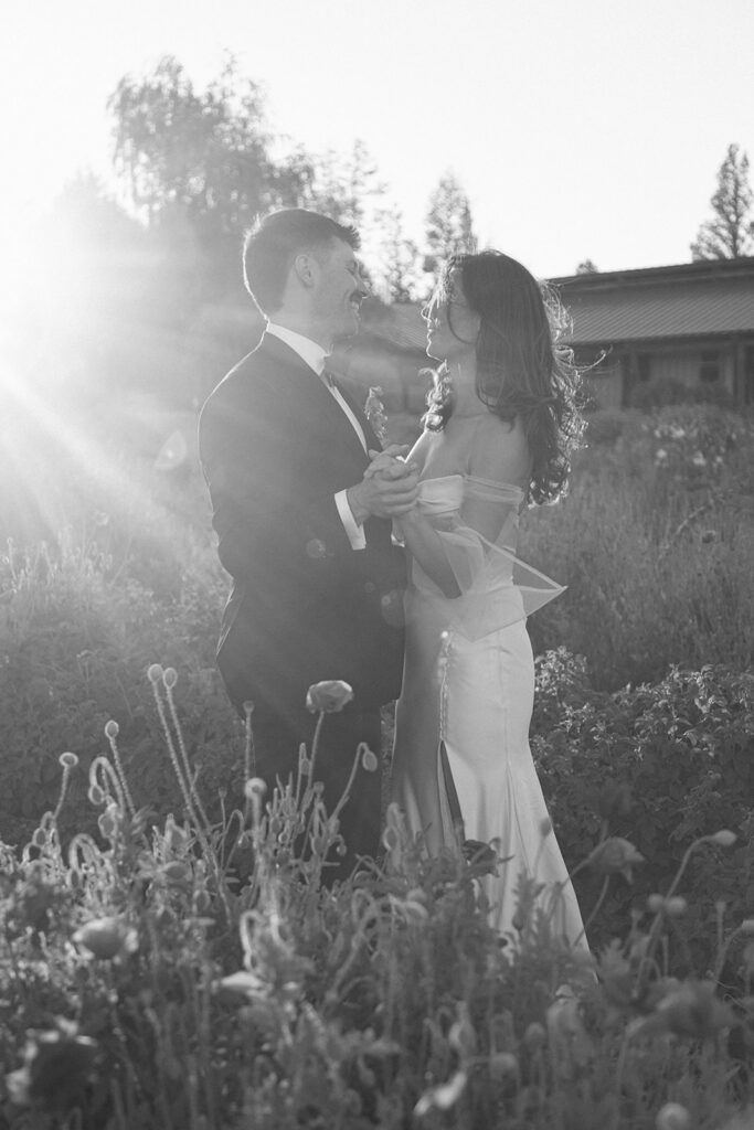 Black and white film photo of bride and groom holding hands and smiling at each other in a poppy field